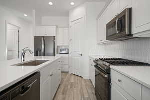 Kitchen with tasteful backsplash, appliances with stainless steel finishes, sink, and white cabinets