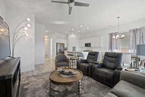 Living room with ceiling fan with notable chandelier and light hardwood / wood-style floors