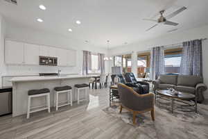 Living room with ceiling fan with notable chandelier and light hardwood / wood-style floors