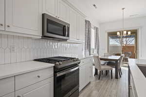 Kitchen featuring tasteful backsplash, an inviting chandelier, hanging light fixtures, appliances with stainless steel finishes, and white cabinets