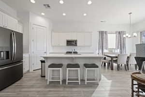 Kitchen featuring appliances with stainless steel finishes, tasteful backsplash, white cabinets, hanging light fixtures, and a center island with sink