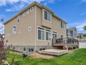 Rear view of house featuring a deck, a lawn, and stucco siding