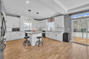 Kitchen with white cabinetry, sink, a kitchen breakfast bar, a center island, and black appliances