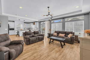 Living room with sink, a tray ceiling, light hardwood / wood-style floors, and a chandelier