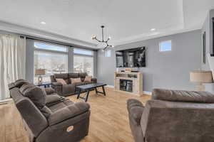 Living room featuring a notable chandelier, a tray ceiling, a wealth of natural light, and light wood-type flooring