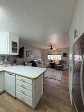 Kitchen featuring refrigerator location, white cabinetry, dishwashing machine, kitchen peninsula, and light hardwood / wood-style flooring