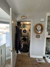 Laundry room with hardwood / wood-style flooring, stacked washer / dryer location, and a textured ceiling