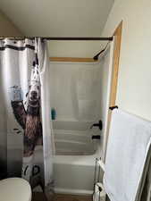 Bathroom with shower / bath combination with curtain, toilet, and a textured ceiling