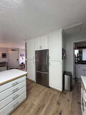 Kitchen featuring refrigerator location, white cabinetry, light hardwood / wood-style floors, and a textured ceiling