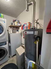 Washroom with water heater, stacked washer and clothes dryer location, and a textured ceiling