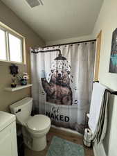 Bathroom featuring wood-type flooring, walk in shower, a textured ceiling, and toilet