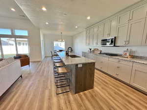 Kitchen with sink, appliances with stainless steel finishes, a kitchen breakfast bar, an island with sink, and light stone countertops