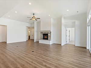 Unfurnished living room featuring ceiling fan, a stone fireplace, and light hardwood / wood-style flooring