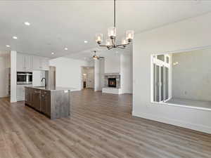 Kitchen with decorative light fixtures, sink, a kitchen island with sink, stainless steel oven, and light hardwood / wood-style floors