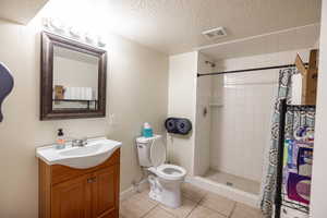 Bathroom with toilet, a textured ceiling, tile patterned floors, a shower with shower curtain, and vanity