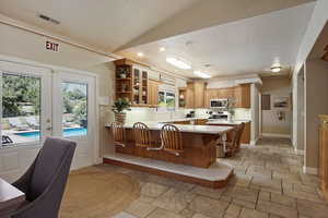 Kitchen with vaulted ceiling, appliances with stainless steel finishes, a breakfast bar, kitchen peninsula, and french doors