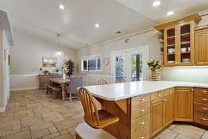 Kitchen featuring french doors, lofted ceiling, a breakfast bar area, decorative light fixtures, and kitchen peninsula