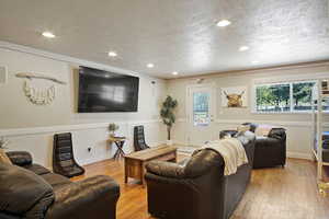 Living room with crown molding, a textured ceiling, and light wood-type flooring