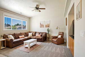 Living room with ceiling fan, vaulted ceiling, and light carpet