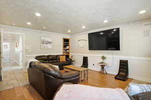 Living room with ornamental molding, a textured ceiling, and light wood-type flooring