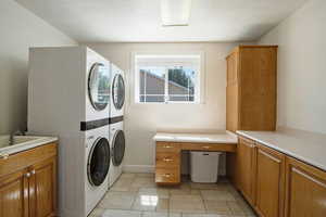 Clothes washing area featuring stacked washer and dryer, sink, and cabinets