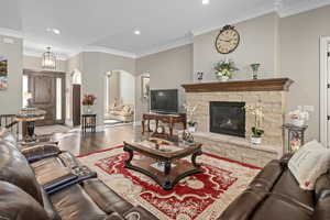 Living room with crown molding, a stone fireplace, and hardwood / wood-style floors