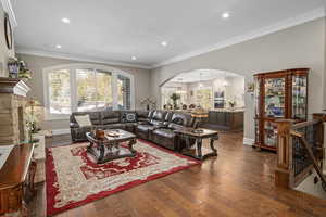 Living room with crown molding, dark wood-type flooring, and a stone fireplace