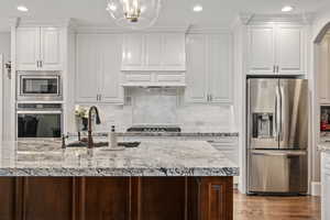 Kitchen featuring sink, white cabinetry, light stone counters, stainless steel appliances, and backsplash