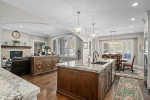 Kitchen featuring sink, light stone counters, pendant lighting, a fireplace, and a kitchen island with sink