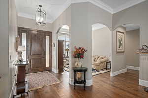 Foyer with an inviting chandelier, dark wood-type flooring, and ornamental molding