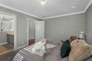 Carpeted bedroom with ensuite bath and ornamental molding