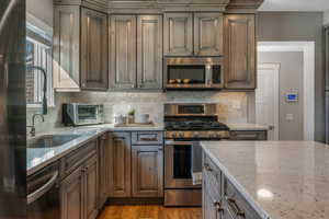 Kitchen with dark brown cabinets, light wood-type flooring, appliances with stainless steel finishes, light stone countertops, and backsplash