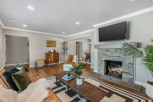 Living room with wood-type flooring, a stone fireplace, and ornamental molding