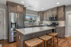 Kitchen with sink, appliances with stainless steel finishes, dark hardwood / wood-style floors, a center island, and light stone counters