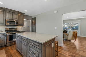 Kitchen with stainless steel appliances, dark hardwood / wood-style floors, tasteful backsplash, light stone counters, and a kitchen island