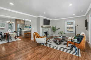 Living room featuring crown molding, dark hardwood / wood-style flooring, a stone fireplace, and a notable chandelier