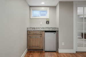 Bar with light stone counters, hardwood / wood-style flooring, and stainless steel fridge