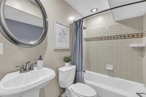 Full bathroom with sink, shower / bathtub combination with curtain, and toilet