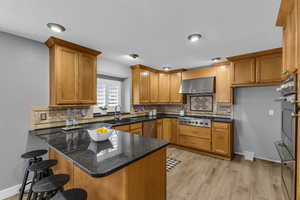 Kitchen featuring wall chimney exhaust hood, sink, dark stone countertops, appliances with stainless steel finishes, and kitchen peninsula