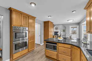 Kitchen with appliances with stainless steel finishes, light wood-type flooring, and dark stone counters