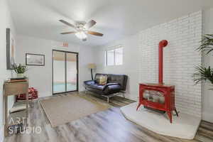 Sitting room featuring ceiling fan, brick wall, hardwood / wood-style floors, and a wood stove