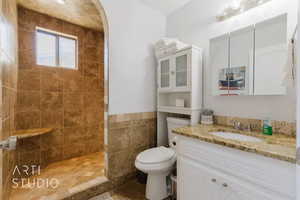 Bathroom with tile walls, vanity, toilet, and tiled shower