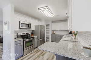 Kitchen with appliances with stainless steel finishes, tasteful backsplash, white cabinets, kitchen peninsula, and light hardwood / wood-style flooring