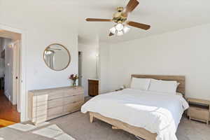 Carpeted bedroom featuring ensuite bath and ceiling fan