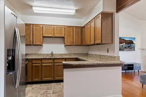 Kitchen featuring stainless steel fridge with ice dispenser, sink, beam ceiling, kitchen peninsula, and a textured ceiling