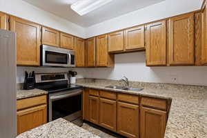 Kitchen with stainless steel appliances, sink, and light stone counters