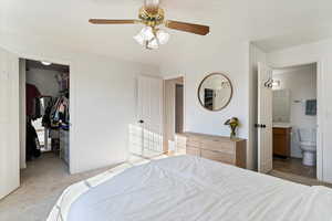 Bedroom featuring ensuite bath, a spacious closet, light carpet, a closet, and ceiling fan