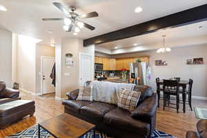 Living room featuring beam ceiling, ceiling fan with notable chandelier, and light wood-type flooring