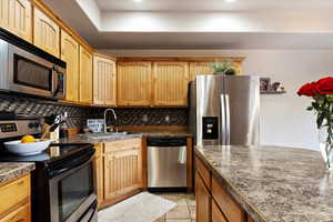 Kitchen with sink, backsplash, light tile patterned flooring, and appliances with stainless steel finishes