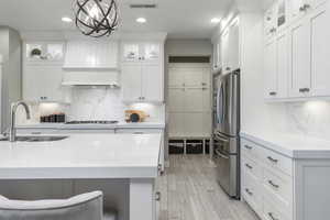 Kitchen with pendant lighting, sink, stainless steel refrigerator, premium range hood, and white cabinets